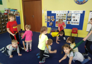 Dzieci na dywanie bawią się w pieski i ich właścicieli. jedne paceruja na czworaka i maja szarfy - smycze, drugie spacerują trzymając smycz.