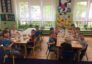Dzieci siedzą przy stole na którym stoją napoje i saatka owocowa z lodami z okazji Dnia Dziecka.