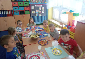 dzieci siedzą przy stołach, świętują urodziny kolegi