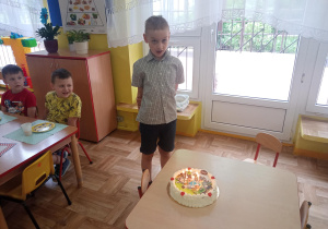 chłopiec stoi przy stoliku, na stoliku leży tort, na nim palą się świeczki