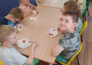 przy stolikach siedzą dzieci, jedzą lody z truskawkami