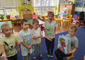 Chłopiec siedzi na krześle, dzieci w półkolu śpiewają "100 lat".