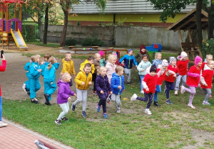 grupa dzieci na podwórku przedszkolnym, wykonują ćwiczenia gimnastyczne