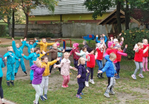 grupa dzieci na podwórku przedszkolnym, wykonują ćwiczenia gimnastyczne