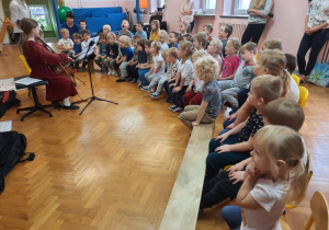 Przedszkolaki siedzą i słuchają koncertu muzycznego.