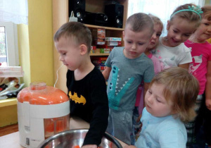 Chłopiec wkłada marchewkę do sokowirówki.