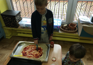 chłopiec stoi przy stoliku, na którym widać pizzę