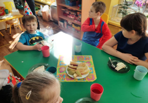 Dzieci siedzą przy stole i zjadają tort.
