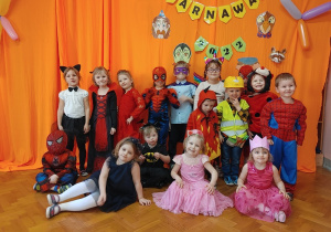 grupa dzieci w przebraniach karnawałowych pozuje do zdjęcia na tle pomarańczowej dekoracji