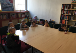 Dzieci siedzą przy stole w bibliotece.