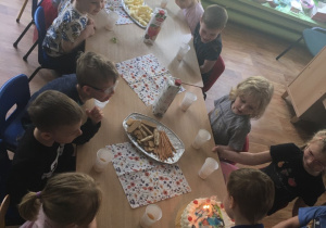 Dzieci siedzą przy stole, a jeden z nich zdmuchuje świeczki.