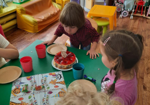 Dzieci siedzą przy stole, a chłopiec zdmuchuje świeczkę.