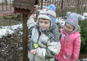 Dzieci w ogródku przedszkolnym dokarmiają ptaki.