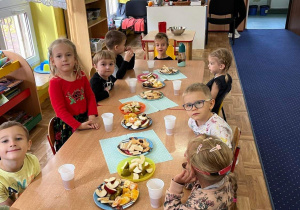 dzieci siedzą przy stolikach, na których są owoce i smakołyki