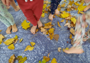 Dzieci spacerują po foli bąbelkowej na której są rozsypane liście.