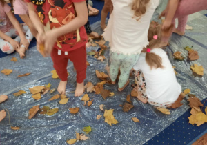Dzieci spacerują po foli bąbelkowej na której są rozsypane liście.