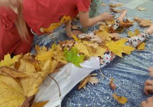 Dzieci obsypują koleżankę liśćmi.