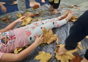 Dzieci obsypują koleżankę liśćmi.