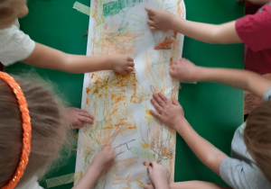 Dzieci kolorują karton kredkami pastelowymi pod którym leżą liście.