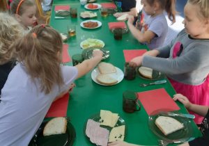 Dzieci siedzą przy stole i samodzielnie przygotowują sobie kanapki.
