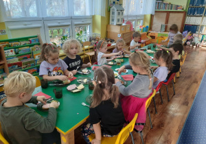 Dzieci siedzą przy stole i samodzielnie przygotowują sobie kanapki.