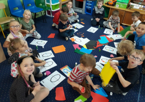 Dzieci siedzą na dywanie i ozdabiają literę "O,O".