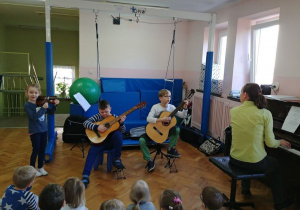 Dziewczynka gra na skrzypcach, dwóch chłopców gra na gitarze.