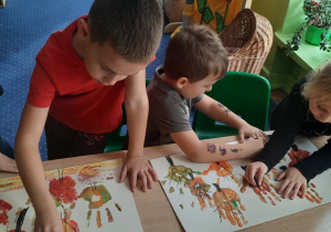 Dzieci przy stoliku odciskają dłonie pomalowane farbami.