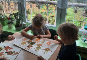 Dzieci przy stoliku dorysowuj pnie drzew do odciśniętej dłoni w farbie.
