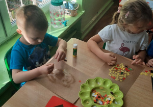 Dzieci przy stoliku wyklejają listkami sowę.