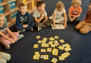 Dzieci siedzą w kole na dywanie i poznają literę "i, i".