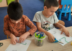 Dzieci siedzą przy stole i wylepiają włóczką literę "I, i".