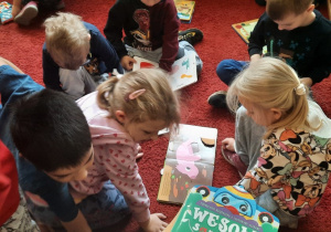 Dzieci na dywanie w bibliotece oglądają książki.