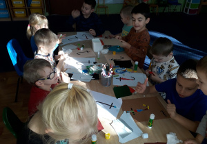 Dzieci siedzą przy stole i wykonują wydzierankę z kolorowego papieru.