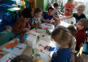 Dzieci siedzą przy stole i wykonują wydzierankę z kolorowego papieru.