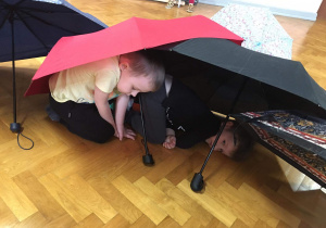 Dzieci na sali gimnastycznej bawią się z wykorzystaniem parasolek.