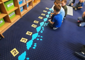 Dzieci siedzą na dywanie i przyporządkowują ilość kropli z chmur do cyfr.