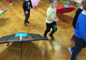 Dzieci na sali gimnastycznej bawią się z wykorzystaniem parasolek.