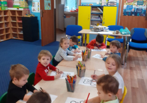 Dzieci siedzą przy stole i kolorują misia.