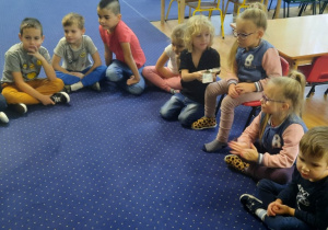 Dzieci siedzą w kole na dywanie i oglądają banknoty.