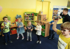 dzieci tańczą w rytm muzyki i wystukują rytm na swoich instrumentach.