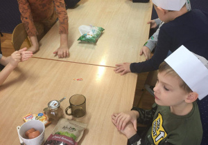 Dzieci siedzą przy stole w kucharskich czapkach.