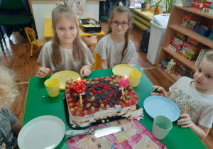 Dziewczynki siedzą przy stole przed nimi stoi tort.
