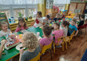 Dzieci siedzą przy stole i zjadają słodkości przygotowane przez mamę dziewczynek.