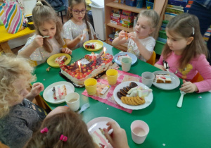 Dzieci siedzą przy stole i zjadają słodkości przygotowane przez mamę dziewczynek