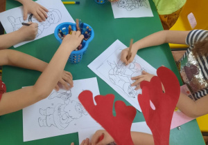 Dzieci siedzą przy stole i kolorują postać Św. Mikołaja.
