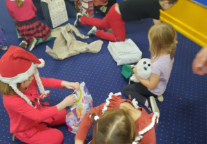 Dzieci siedzą na dywanie i rozpakowują prezenty.