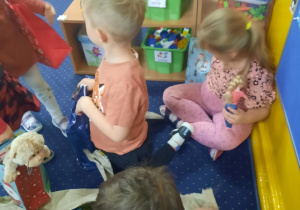 Dzieci siedzą na dywanie i rozpakowują prezenty.
