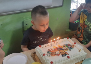 Chłopiec siedzi przed tortem i zdmuchuje świeczki.