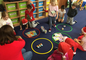 Dzieci na dywanie rozwiązują matematyczne zadania mikołajkowe.